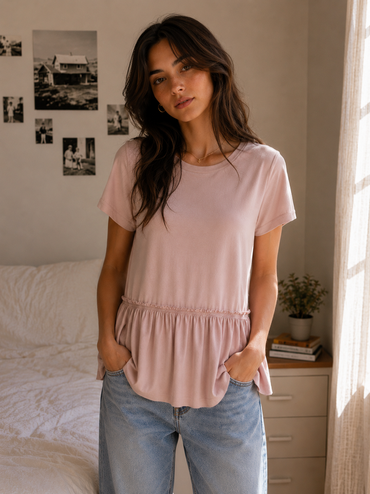 Woman wearing a blush pink short sleeve peplum top with light wash jeans.