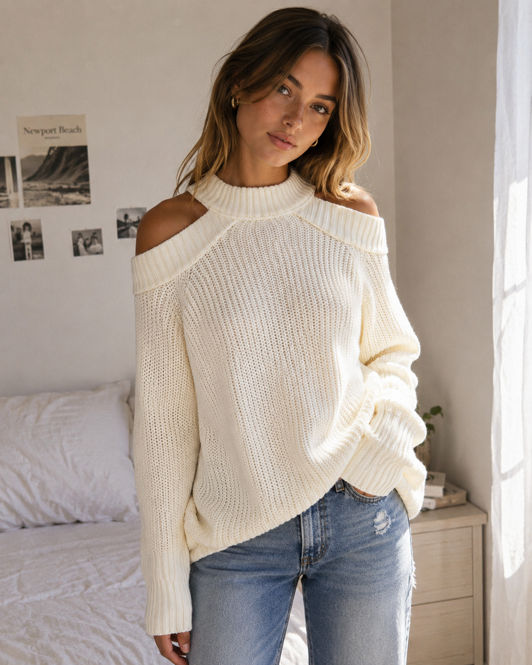 Woman wearing an ivory cold shoulder knit sweater with mock neck and open back.