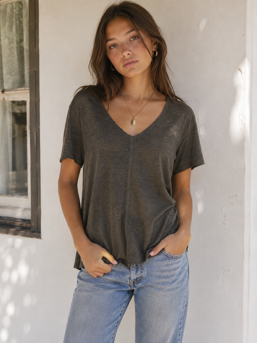 Model wearing an army green relaxed V-neck tee with a center seam and light wash jeans.