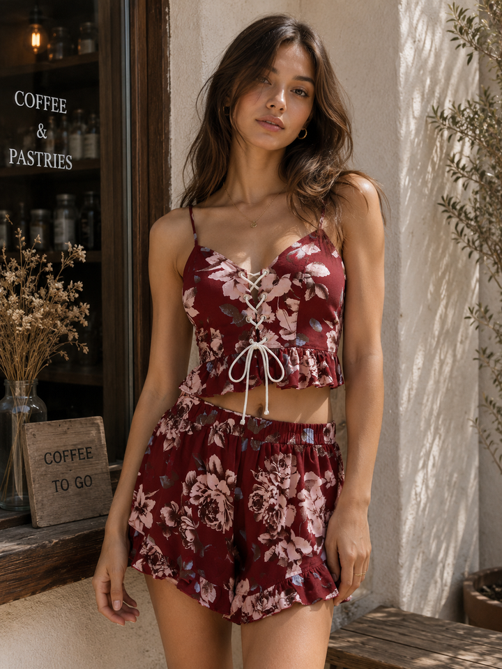 Model wearing a burgundy floral two-piece set featuring a lace-up crop top with ruffle hem and matching floral shorts.
