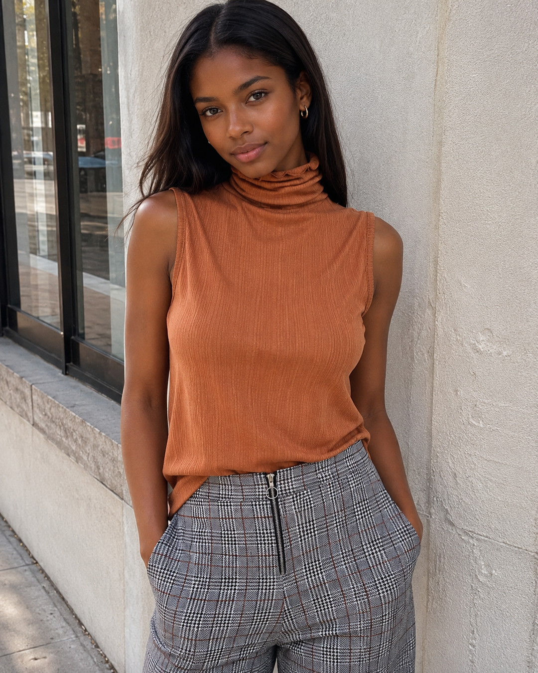 Sleeveless ribbed turtleneck knit top in Gucci Tan styled with high-waisted plaid pants, front view.
