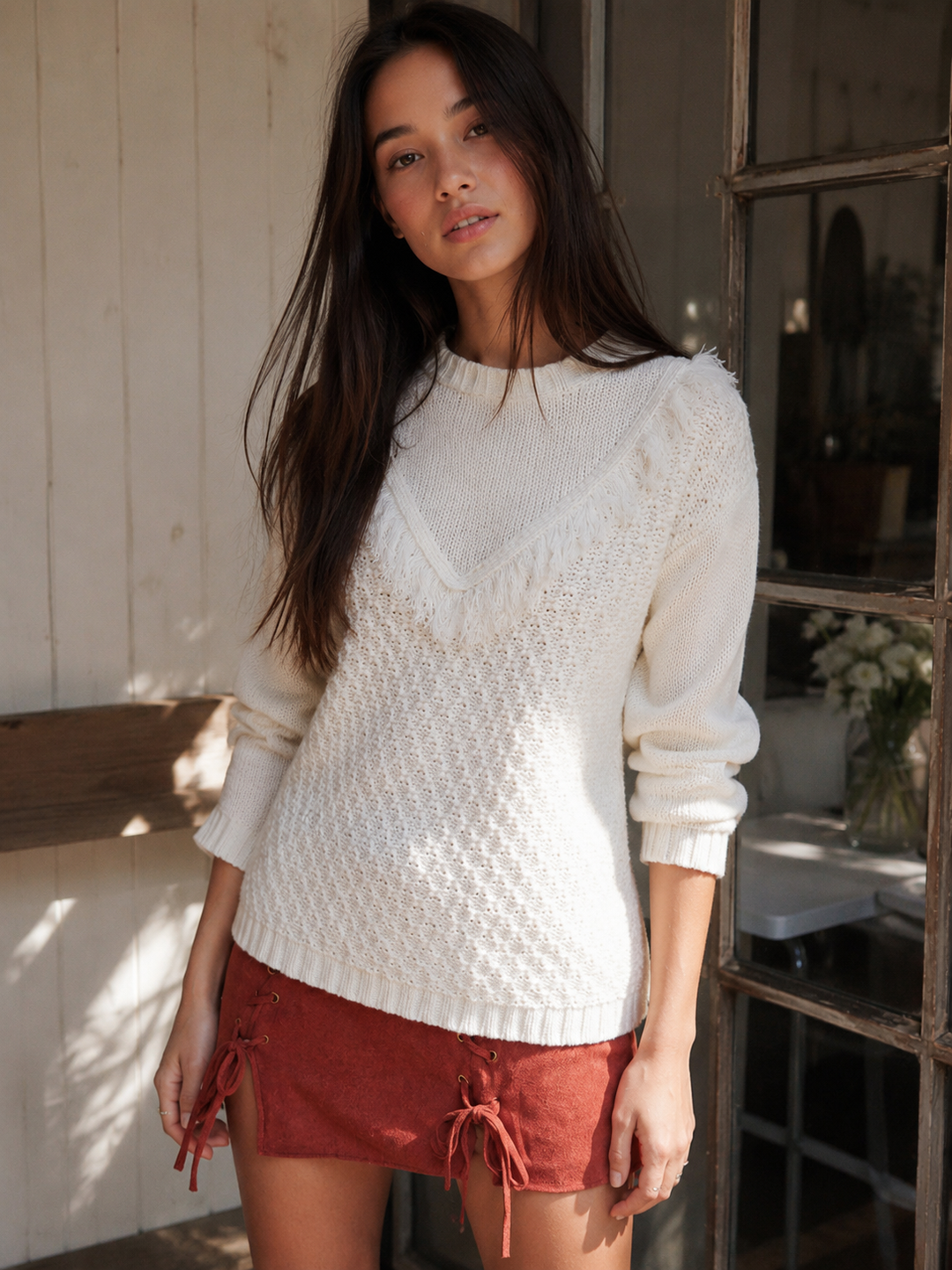 Ivory pointelle knit sweater with V-shaped fringe trim, crew neckline and long sleeves styled with a rust mini skirt.
