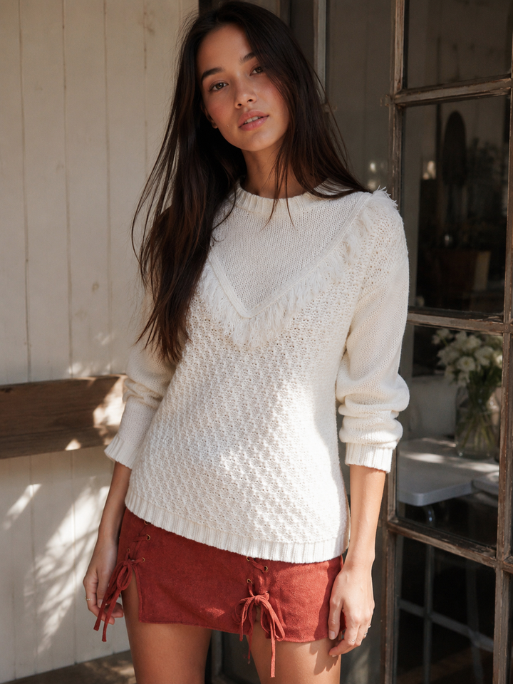 Ivory pointelle knit sweater with V-shaped fringe trim, crew neckline and long sleeves styled with a rust mini skirt.
