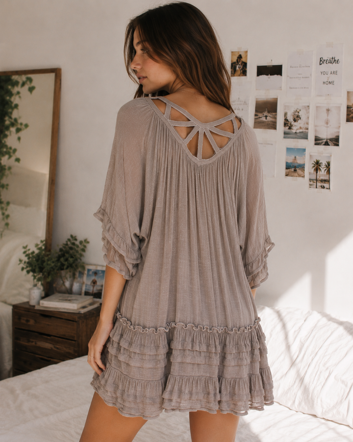 Back view of taupe babydoll dress showcasing intricate strappy back detail and tiered ruffle hem.