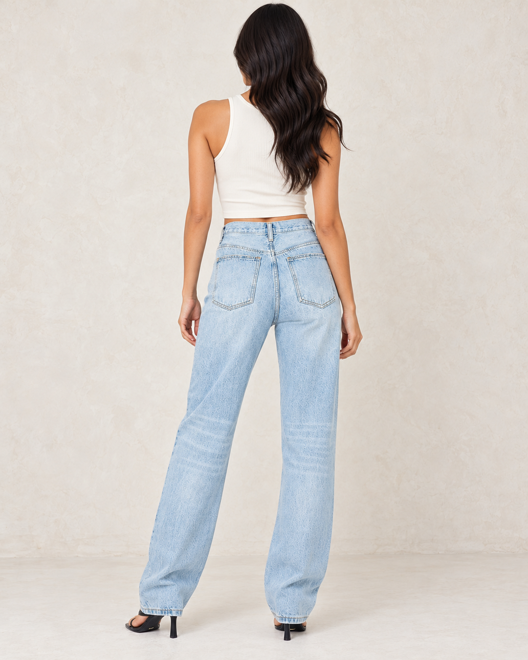 Back view of light-wash asymmetrical wrap-waist denim jeans, showing the rear patch pockets and full-length legs.