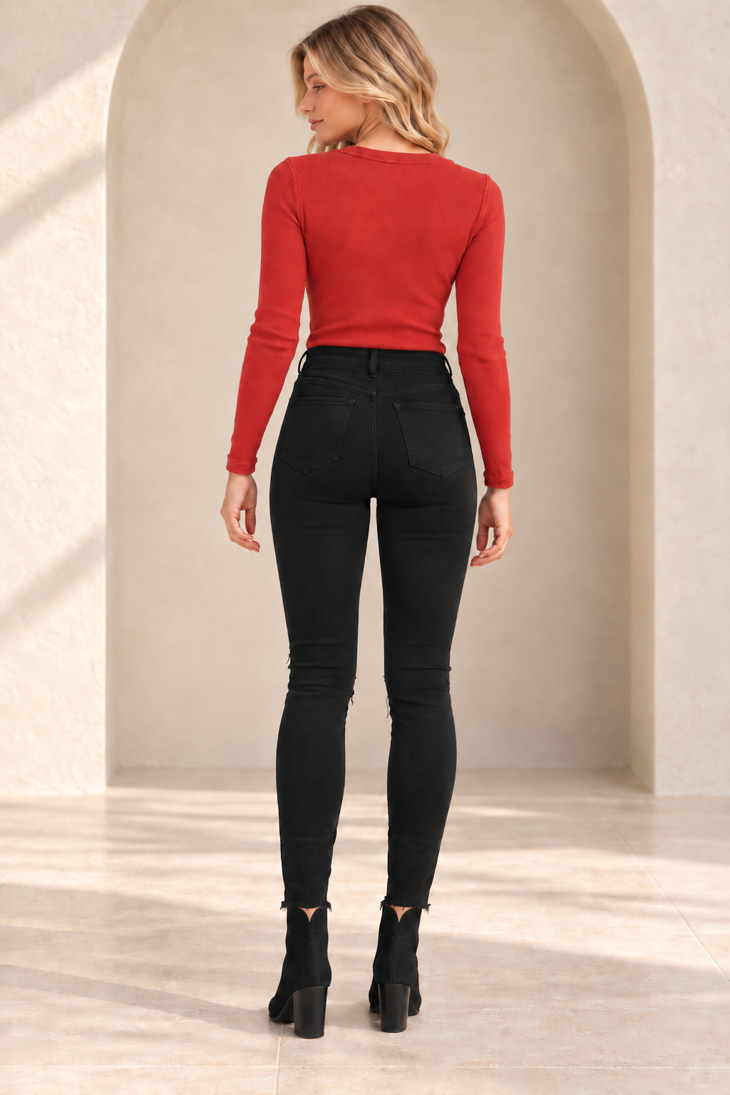 Bella Super High Rise Distressed Black Skinny Jeans, back view on an adult model with a red Free People Call Me Cardi top and black Davinna suede ankle booties.