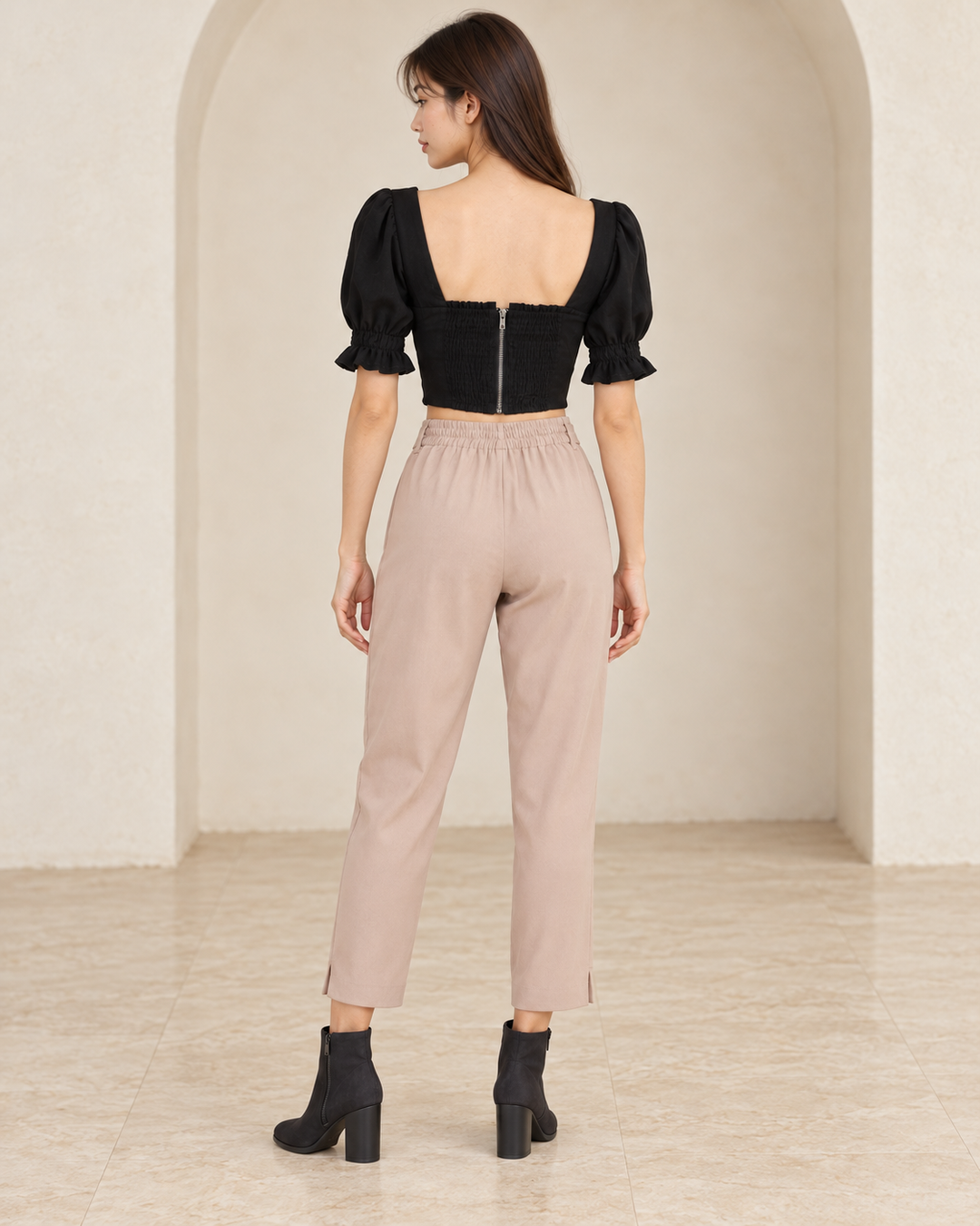 Distraction black bustier cropped blouse, back outfit view showing the smocked panel and center zipper, styled with mauve tie-waist pants and black nubuck ankle boots.