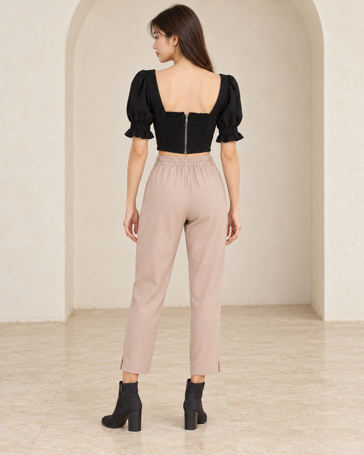 Distraction black bustier cropped blouse, back outfit view showing the smocked panel and center zipper, styled with mauve tie-waist pants and black nubuck ankle boots.