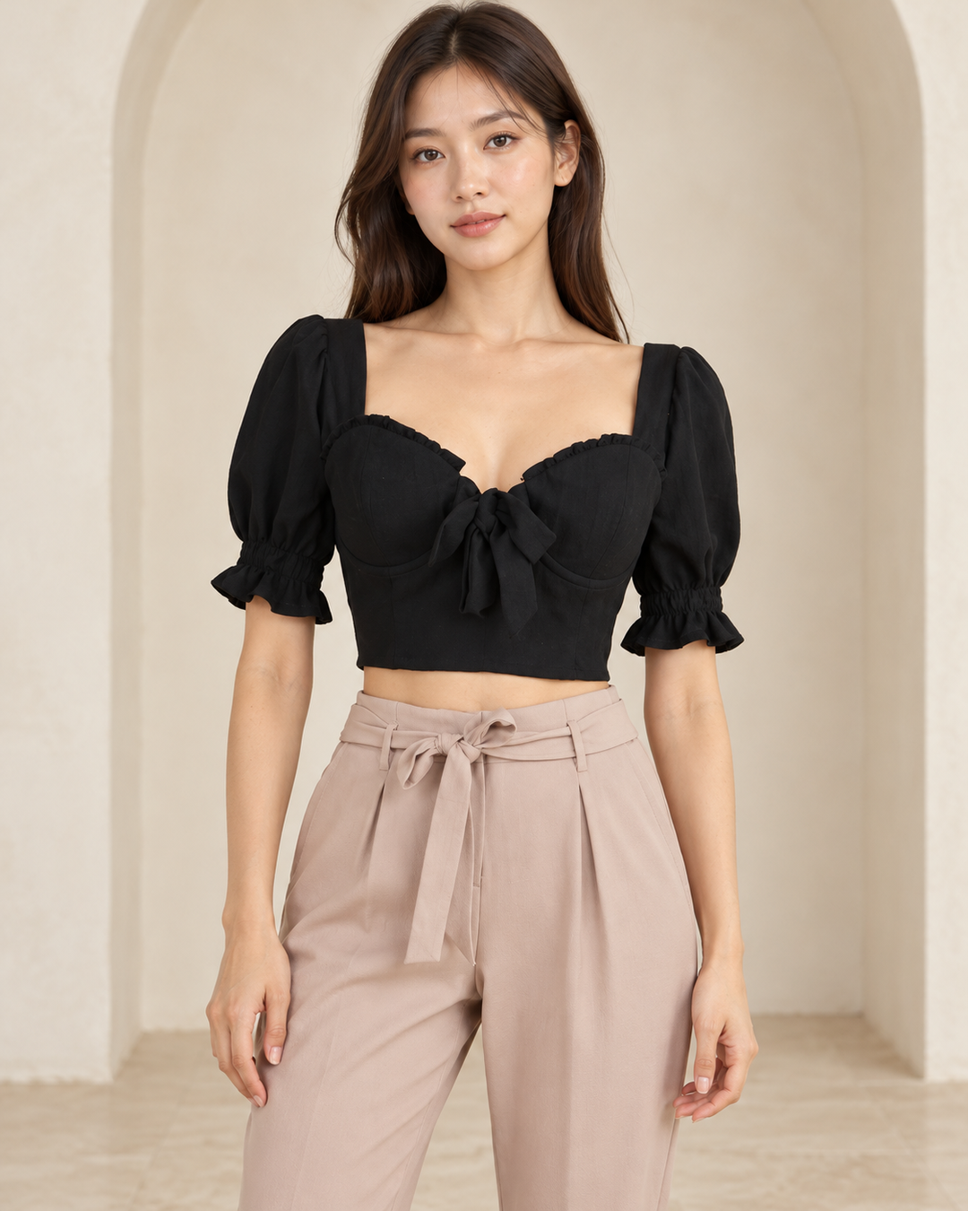Distraction black bustier cropped blouse, front view on a model showing the front tie, puff sleeves and ruffled cuffs, styled with mauve tie-waist pants.