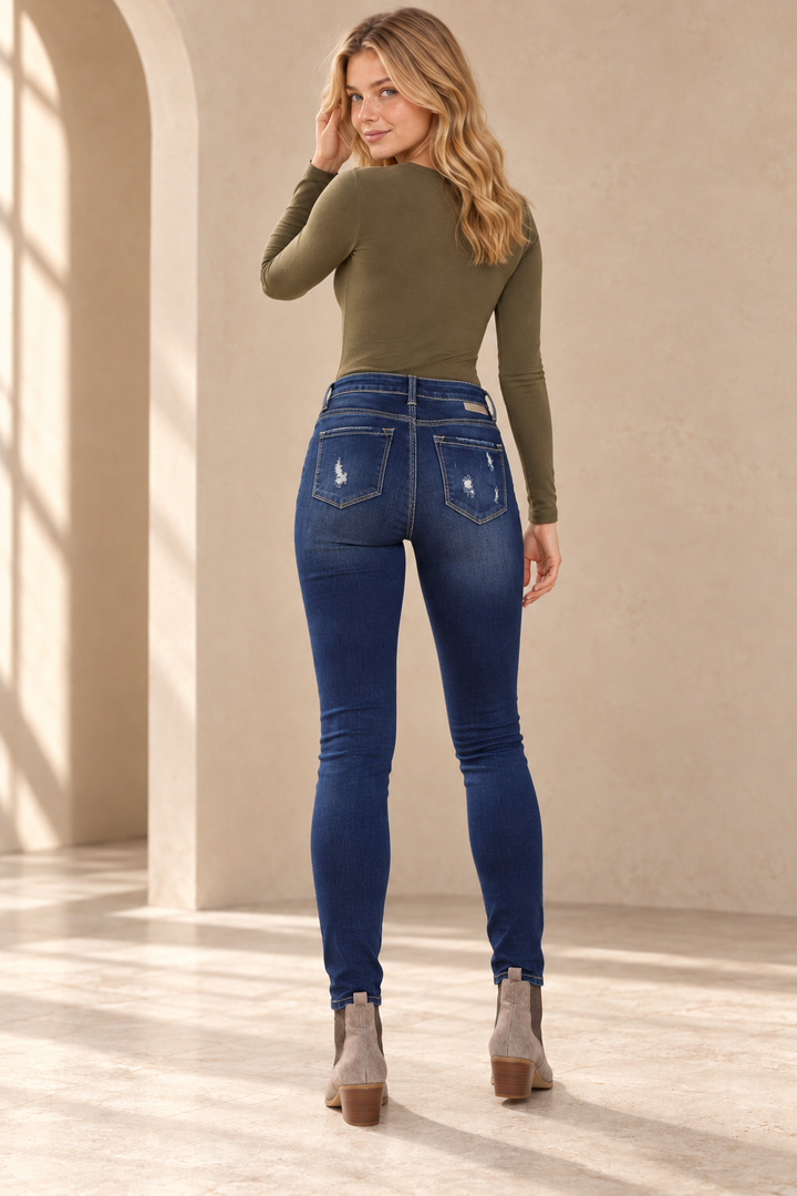 Gemma Faded Medium Wash High Rise Distressed Skinny Jeans, back view on an adult model styled with an olive Rosalie Ribbed Long Sleeve Bodysuit and taupe Very Volatile Raya suede ankle booties, in a warm plaster studio.