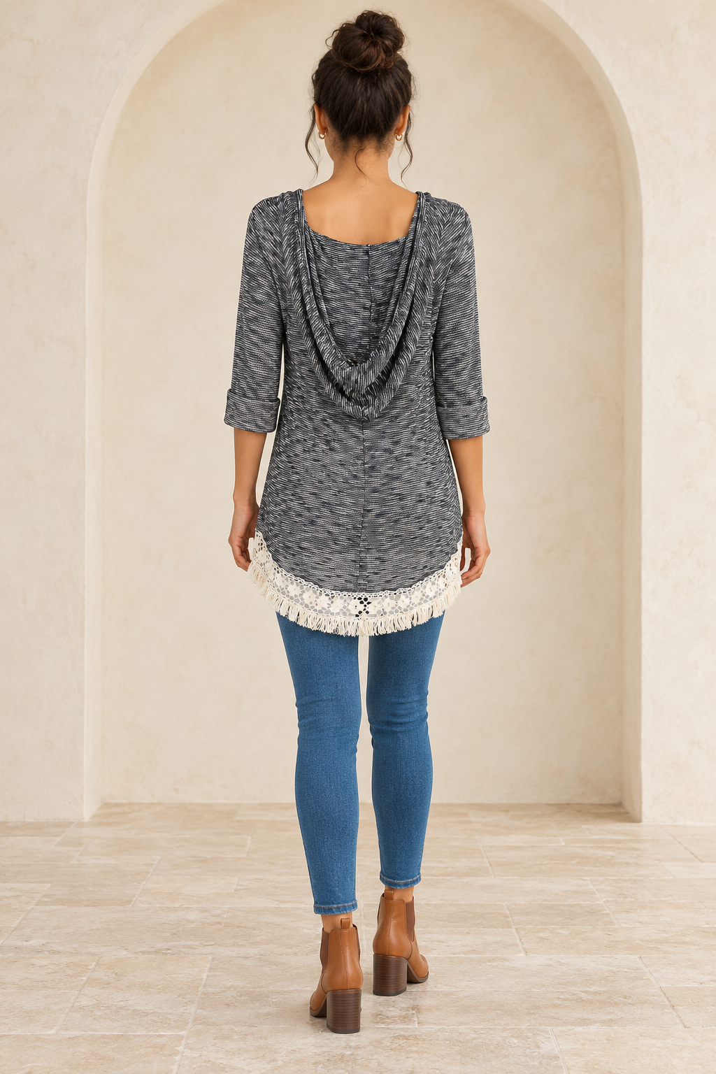 Grey two-tone hooded sweater tunic, back view on a model showing the draped hood and cream lace hem, with medium-blue jeans and camel Chelsea boots.