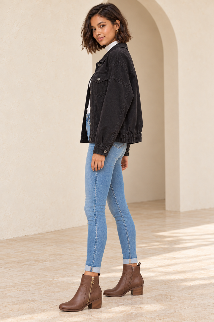 Premium Wash Cotton Denim Jacket in Black, full-length side outfit view showing dropped shoulder, button cuff and gathered rear hem with medium-blue skinny jeans and brown zipper ankle boots.
