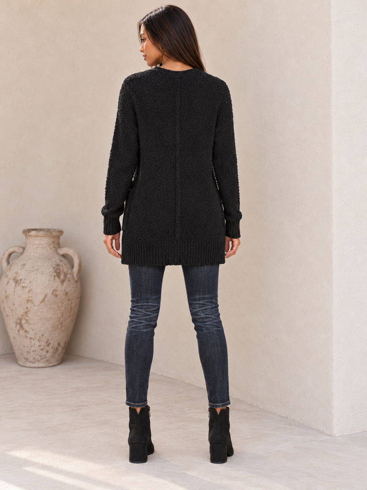 Back view of the black fuzzy pocketed open-front cardigan showing the straight back and long hem.