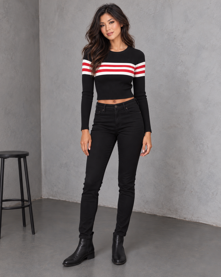 Front view of the black Easy Does It ribbed cropped sweater with two red and three white chest and sleeve stripes, styled with black high-waist denim and Chelsea boots.