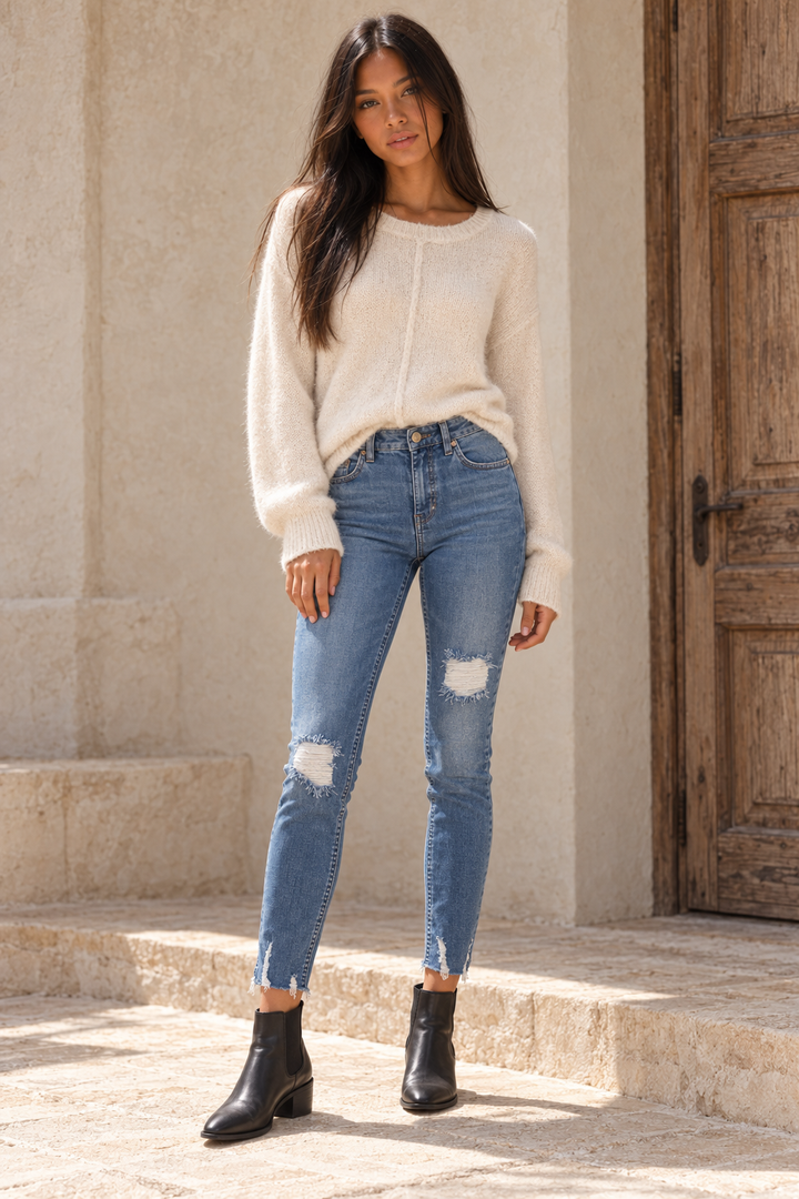 Front view of Free People Blue Shark Bite raw-hem cropped skinny jeans, styled with a cream sweater and black ankle boots.
