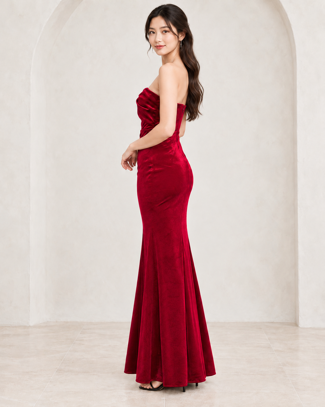 Burgundy twist-front strapless velvet maxi dress, side view showing fitted silhouette and floor-length skirt.