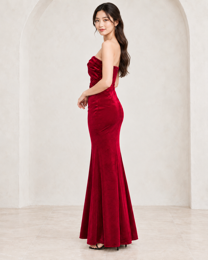 Burgundy twist-front strapless velvet maxi dress, side view showing fitted silhouette and floor-length skirt.