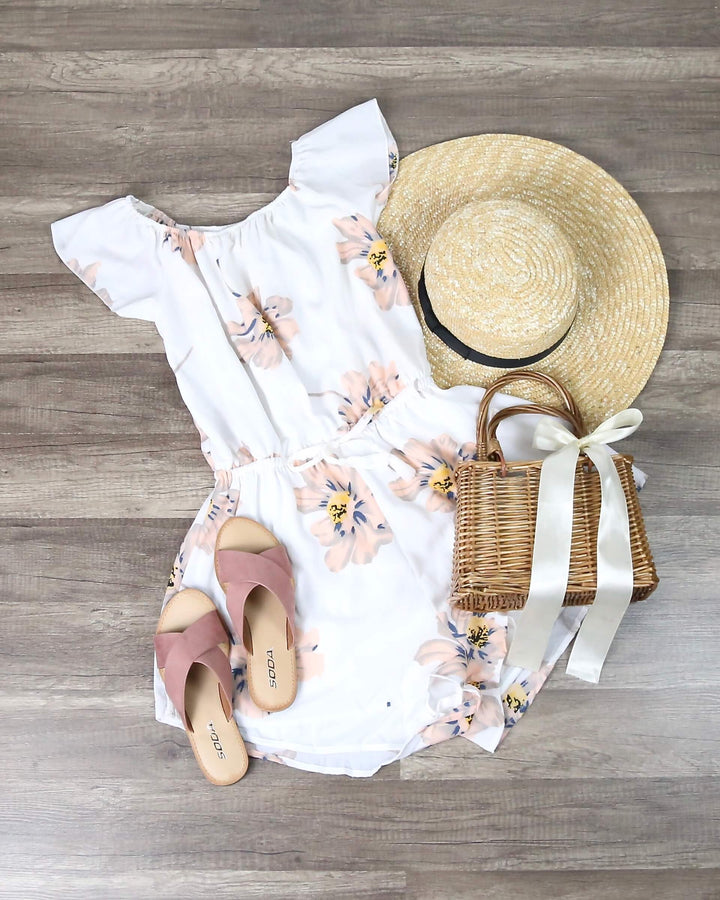 Reverse white off-shoulder romper with peach floral print, laid flat with hat, sandals and bag